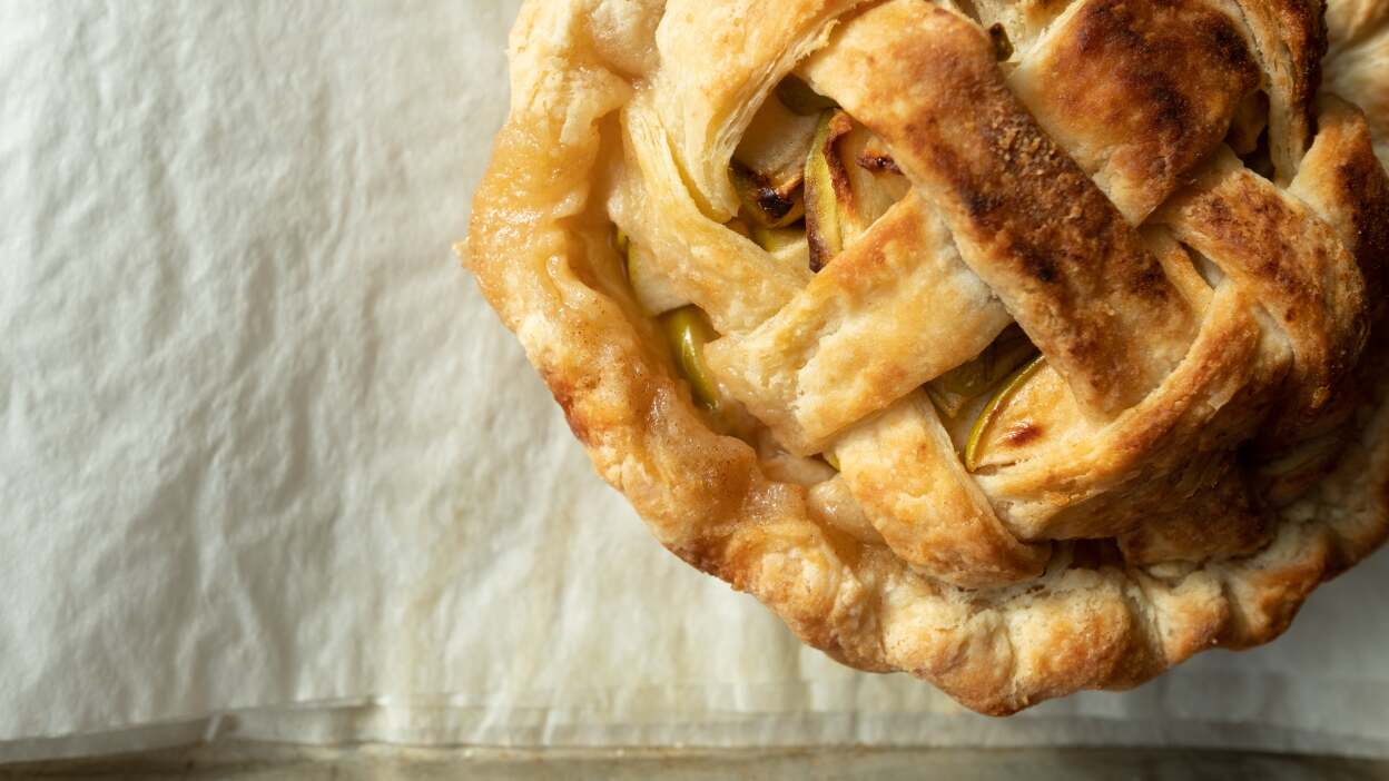 Top-down photo of an apple pie with a lattice crust on a parchment-lined sheet pan. 