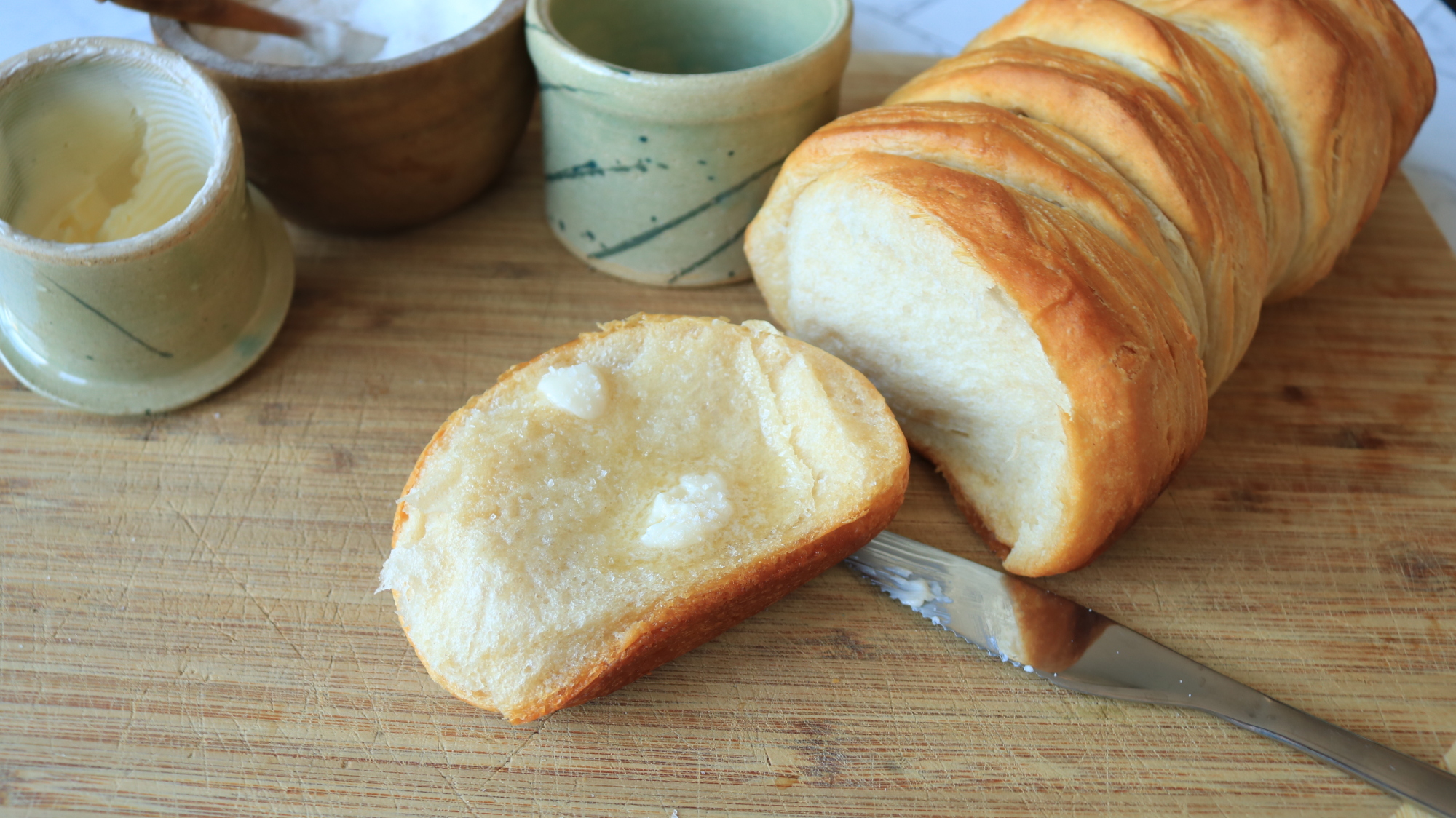 A biscuit with butter on it torn from a loaf.