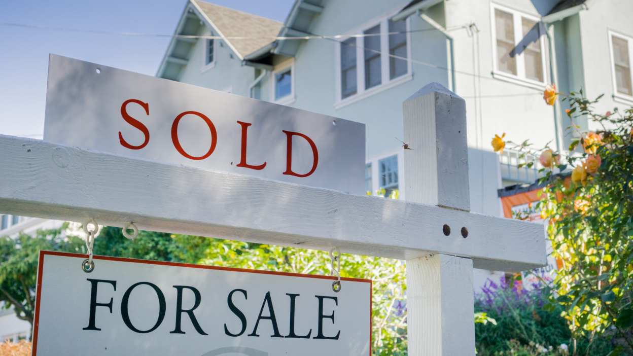 A "sold" sign in front of a large house