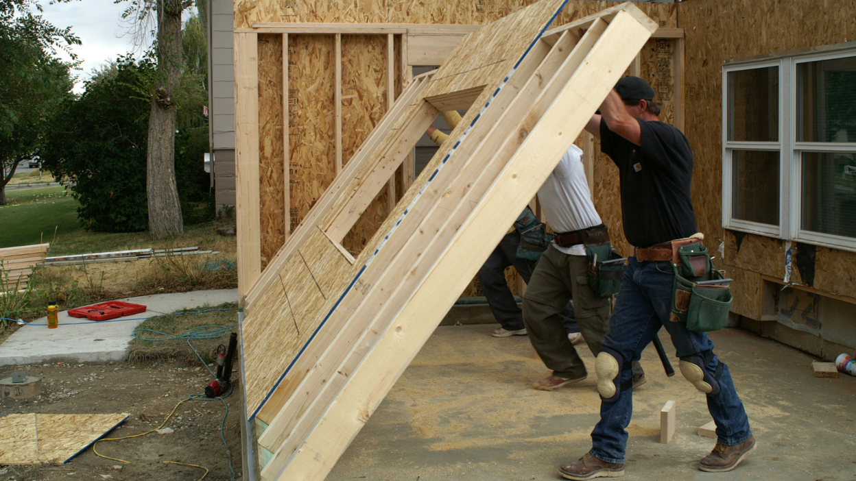 A photograph of workers putting up framing for a new wall in an addition on a house.