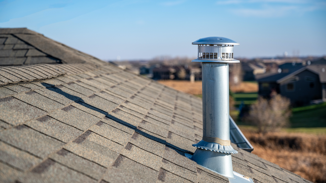 Side view of a metal chimney exhaust on asphalt roof 