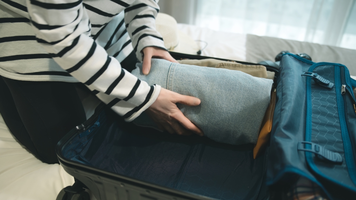 person packing clothes in suitcase