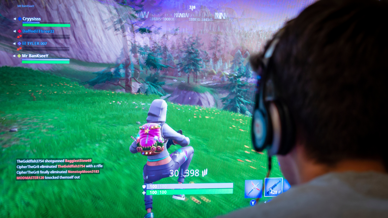 A photo from behind of someone playing Fortnite on a large flatscreen monitor